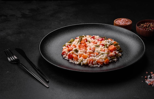 Delicious fresh risotto with vegetables spices and herbs on a black plate on a dark concrete background