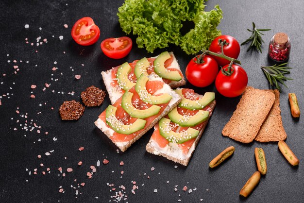 Delicious fresh sandwich with red fish, butter, bread and avocado on a dark concrete table