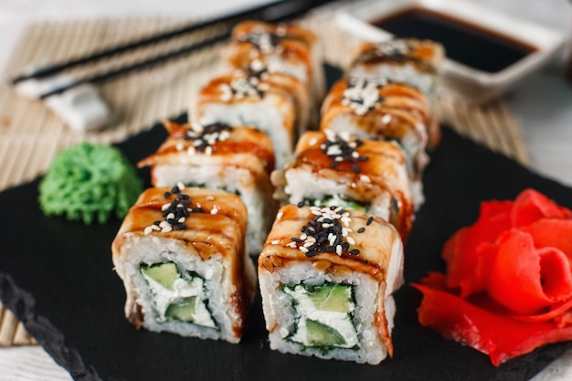 Delicious and fresh set of sushi with cucumber, salmon, eel, avocado and sesame, close up. Yummy rolls served on black slate. Japanese national food.