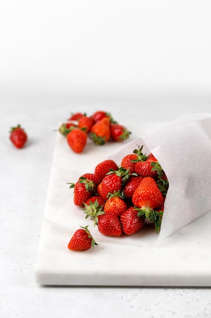 Delicious fresh strawberries in a paper bag on marble board and grey background Berry take away