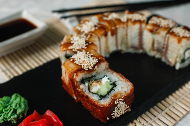 Delicious fresh sushi, uramaki golden dragon roll served on black slate, on straw mat background, closeup. Traditional Japanese food.