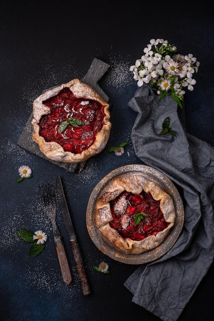 Delicious fresh sweet homemade rustic style strawberry tart with wild flowers on dark textured background