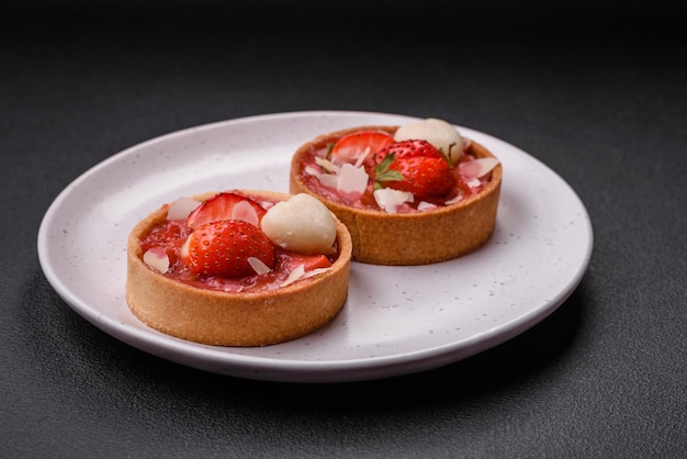 Delicious fresh sweet tartlets with strawberries and coconut flakes on a dark concrete background