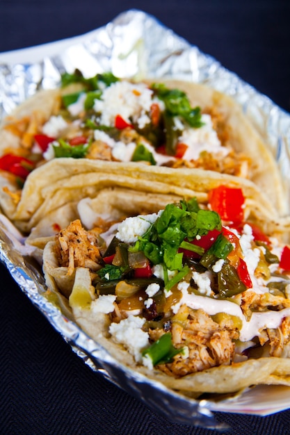 Delicious fresh tacos with chicken crema cilantro green onion and other vegetables in a foil lined