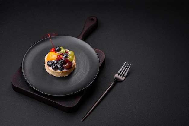 Delicious fresh tart with blueberries cherries grapes on a black ceramic plate