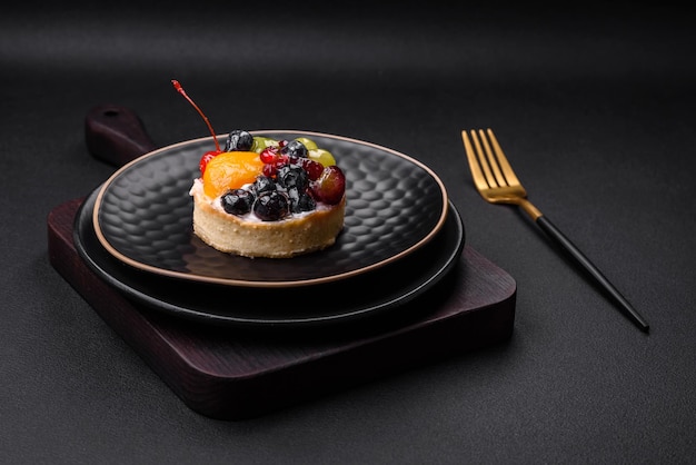 Delicious fresh tart with blueberries cherries grapes on a black ceramic plate