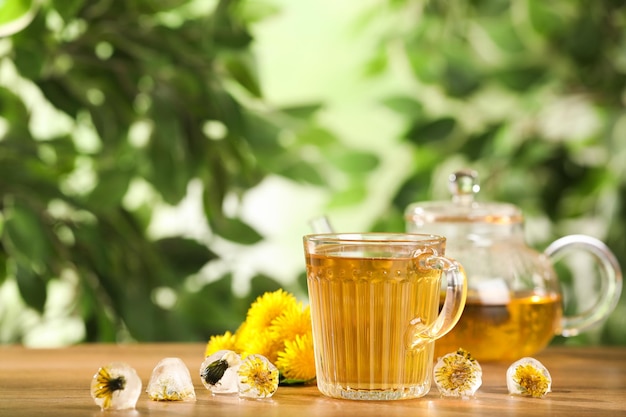 Delicious fresh tea dandelion flowers and ice cubes on wooden table against blurred background Space for text