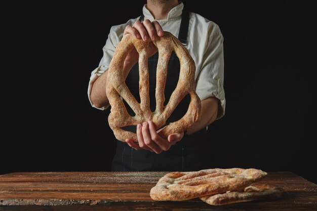 Delicious freshly baked fougas bread in the hands of a man on a black background