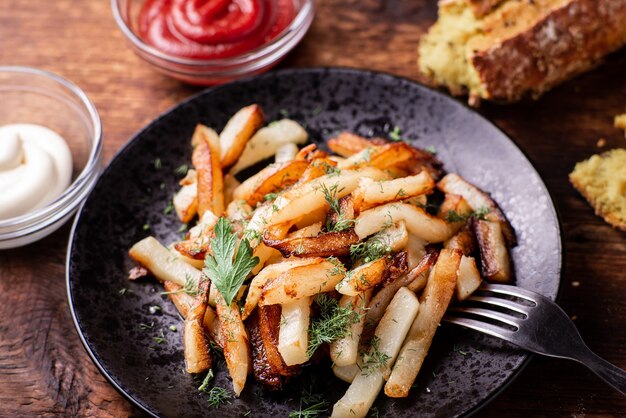 Delicious fried chopped potatoes with ketchup, mayonnaise and herbs on a wooden background.