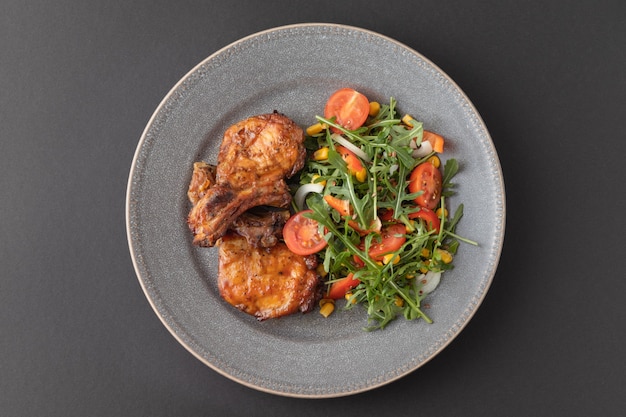 Delicious fried ribs on the plate with fresh vegetable salad Top view Dark table