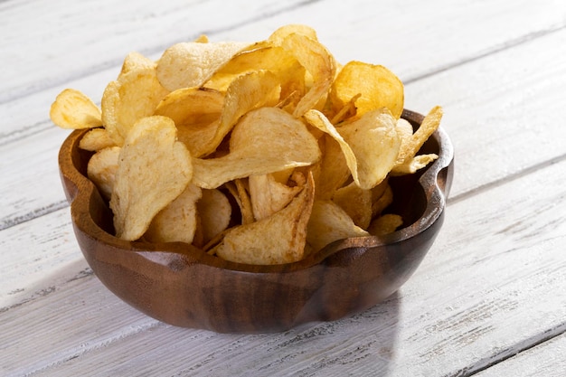 Delicious golden potato chips on a white wooden background.