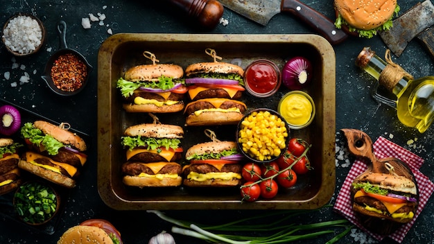 Delicious grilled homemade burgers with beef, tomatoes, cheese, onions and salad. Burger menu. Top view. On a black stone background.