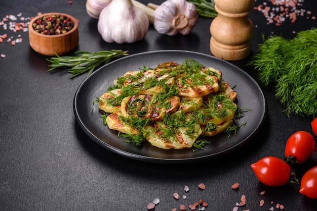 Delicious grilled potato slices with spices and herbs on a black plate