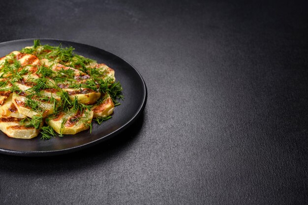 Delicious grilled potato slices with spices and herbs on a black plate