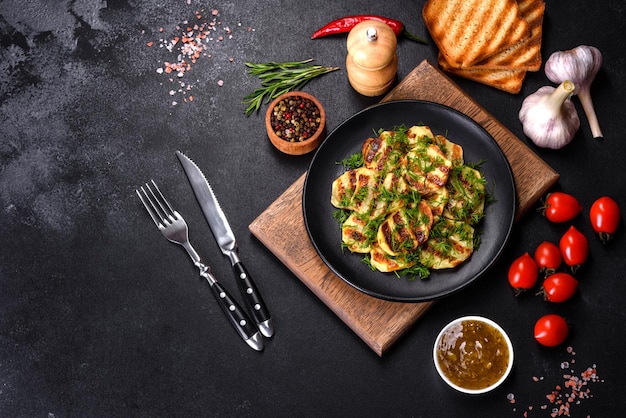 Delicious grilled potato slices with spices and herbs on a black plate