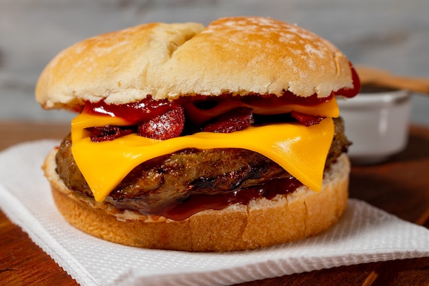 Delicious hamburger with Bacon and cheddar cheese on homemade bread with seeds and ketchup on a wooden surface and rustic background.