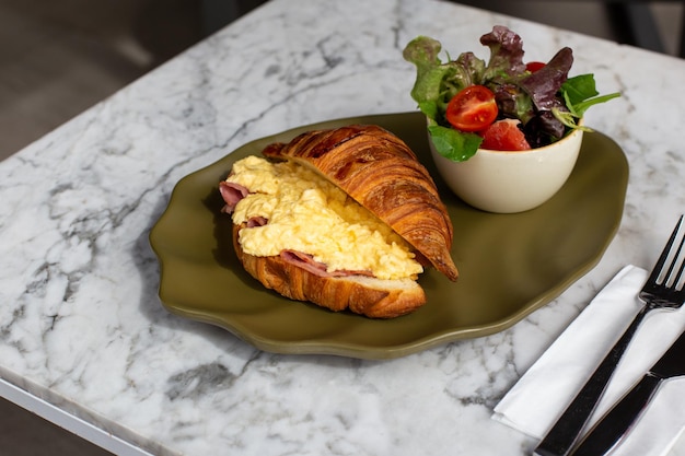 Delicious and healthy breakfast croissant with ham eggs and salad from tomatoes lettuce on green plate