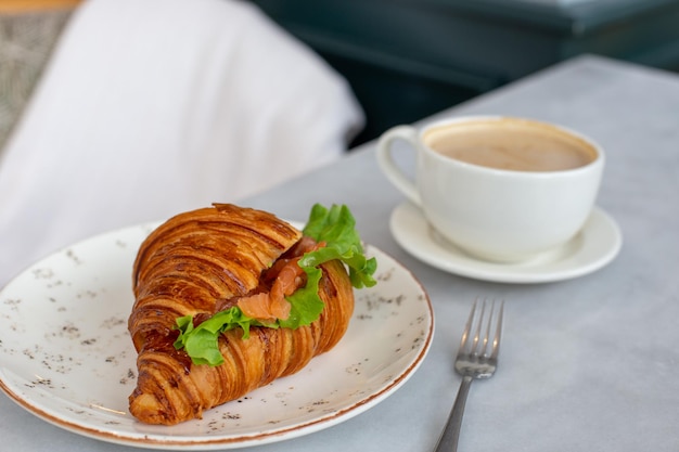 Delicious and healthy breakfast croissant with salmon lettuce and cream cheese on a plate and cappuccino coffee