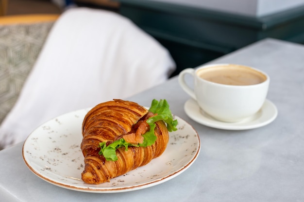 Delicious and healthy breakfast croissant with salmon lettuce and cream cheese on a plate and cappuccino coffee