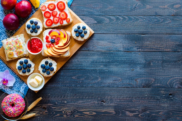 Delicious healthy breakfast fruit sandwiches with different fillings cheese banana strawberry fishing butter blueberry on a different wooden background.