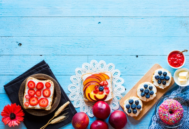 Delicious healthy breakfast, fruit sandwiches with different fillings, cheese, banana, strawberry, fishing, butter, blueberry, on a different wooden background.