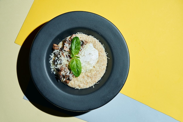 A delicious and healthy breakfast. Oatmeal with poached egg, parmesan and mushrooms in a black plate on s