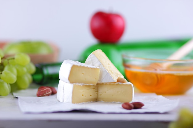 Delicious healthy dish with fruits nuts honey camembert cheese on white parchment Still life of cheese fruit and a green bottle on a blurred background Closeup