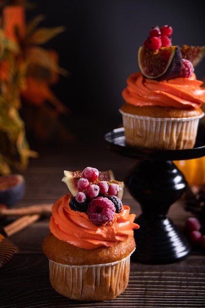 Delicious homemade autumn season spicy pumpkin cupcakes with whipped orange cream with fruit figs and frozen berries