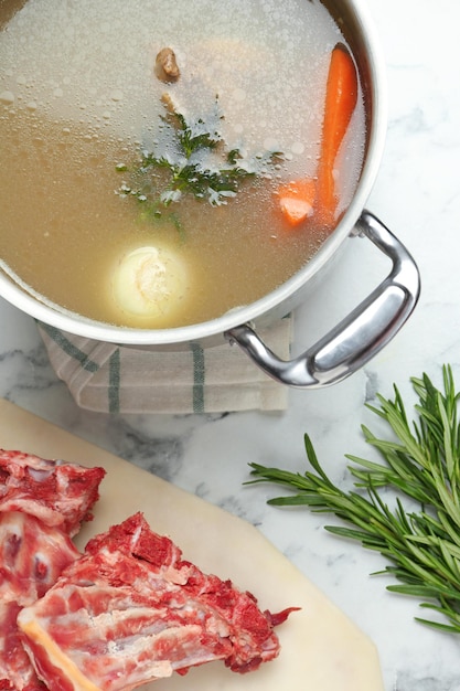 Delicious homemade bone broth and ingredients on white marble table flat lay