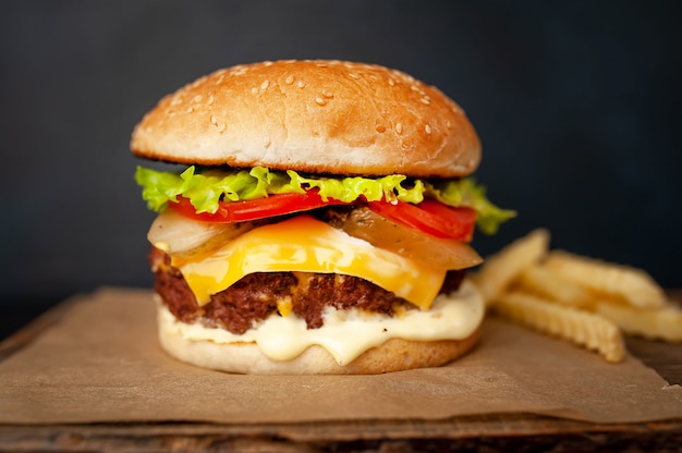 Delicious homemade hamburger with beef, lettuce, cheese, cucumber and french fries on stone background