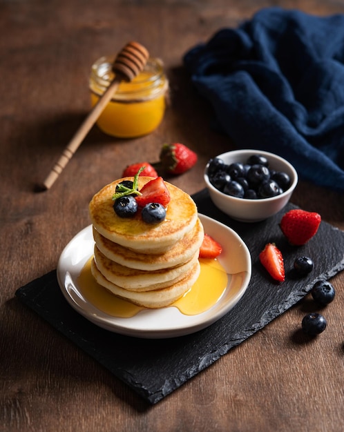 Delicious homemade pancakes with strawberries, blueberries and honey on a dark wooden background with blue napkin. The concept of a healthy and nutritious breakfast. Rustic style. Macro and close up.