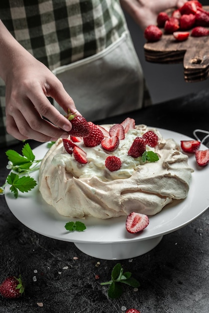 Delicious homemade Pavlova cake with fresh strawberries and whipped cream Female baker decorating delicious meringue cake top view place for text