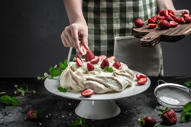 Delicious homemade Pavlova cake with fresh strawberries and whipped cream Female baker decorating delicious meringue cake