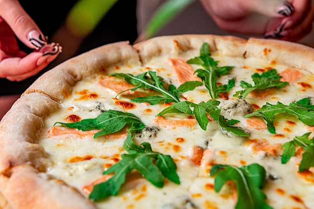 Delicious hot pizza with salmon arugula and different spices on wooden table ready to eat