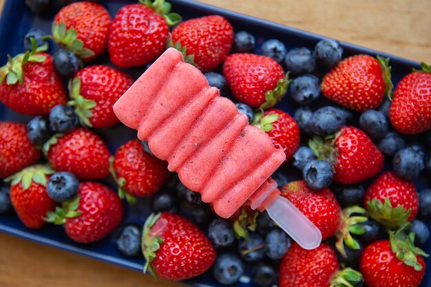 Delicious ice cream from fresh strawberries and blueberries close-up lies on fresh strawberries and blueberries. Assorted background.