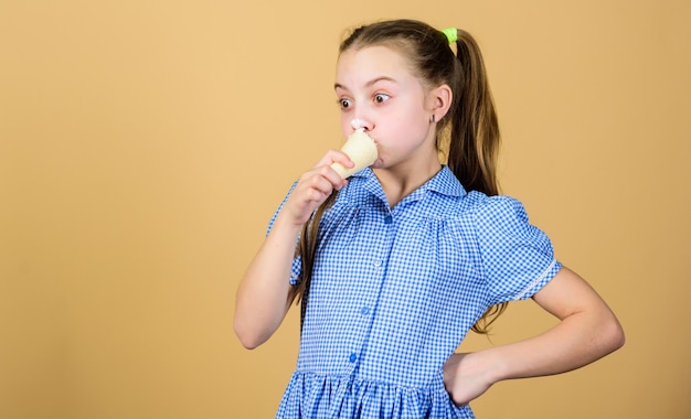 Delicious ice cream Happy childhood Carefree kid enjoy sweet ice cream International childrens day Sweet tooth concept Girl little child eat ice cream cone beige background Summer is here