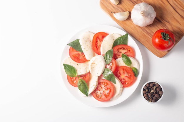 Delicious Italian caprese salad with sliced mozzarella tomatoes basil pesto and garlic on background