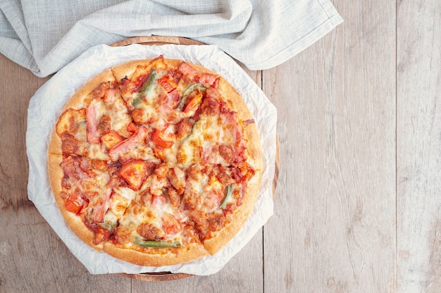 Delicious Italian pizza sliced with bacon, cheese, tomato, capsicum on wooden plate