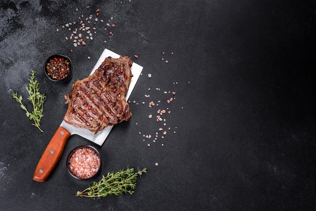 Delicious juicy fresh beef steak with spices and herbs on a dark concrete background. Grilled dishes