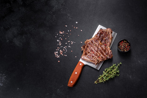 Delicious juicy fresh beef steak with spices and herbs on a dark concrete background. Grilled dishes