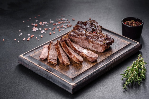 Delicious juicy fresh beef steak with spices and herbs on a dark concrete background. Grilled dishes