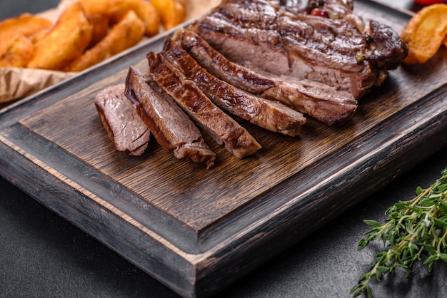 Delicious juicy fresh beef steak with spices and herbs on a dark concrete background. Grilled dishes