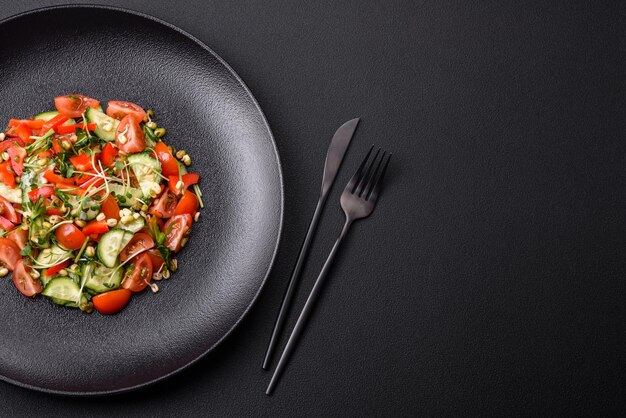 Delicious juicy fresh salad of tomatoes peppers cucumber microgreens and sprouted mung bean on a black ceramic plate on a dark concrete background