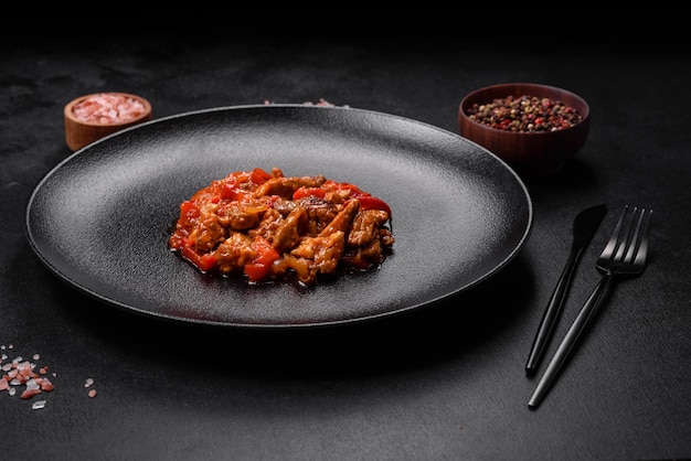 Delicious juicy meat with hot peppers and sauce on a black ceramic plate on a dark concrete background