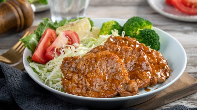 Delicious juicy pork chops with vegetable and fruit salad meal in a plate on dining table.