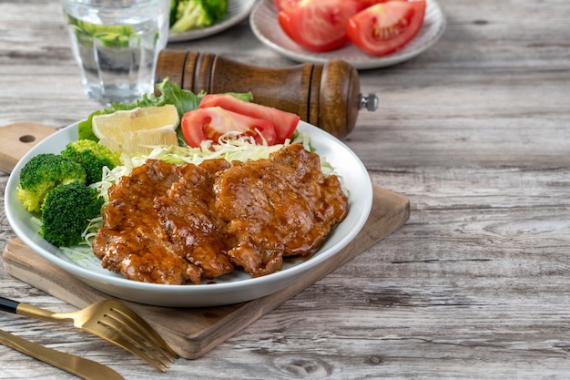 Delicious juicy pork chops with vegetable and fruit salad meal in a plate on dining table.