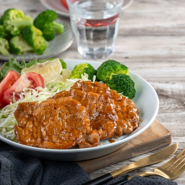 Delicious juicy pork chops with vegetables meal in a plate on dining table.