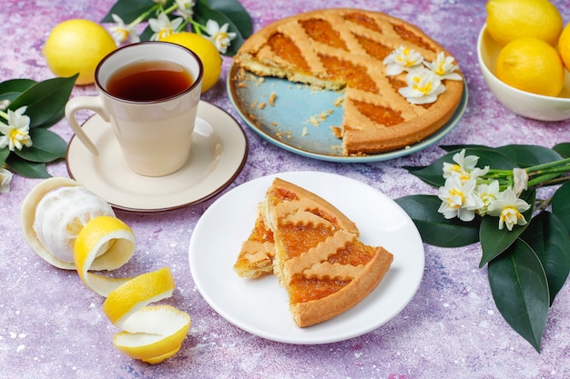 Delicious lemon pie slices with fresh lemons and a cup of tea on concrete, top view