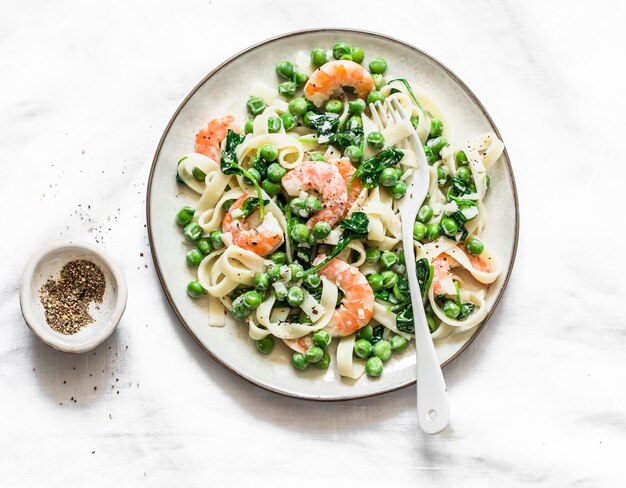 Delicious lunch green peas shrimps spinach cream sauce tagliatelle pasta on a light background