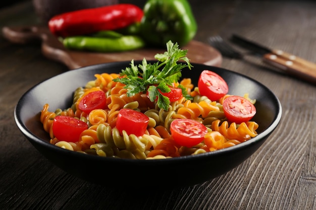 Delicious macaroni dish in black bowl on served wooden table